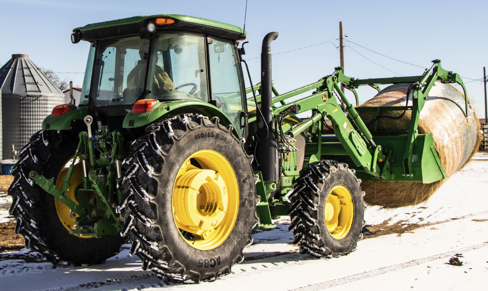 John Deere tractor moving a bale of hay in the snow.